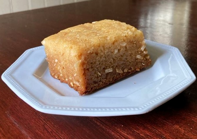 A piece of mochiko cake on a small white ceramic plate.